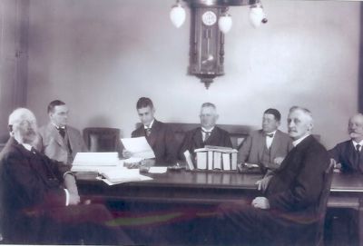 7 män runt sammanträdesbord
Nyckelord: Väggklocka