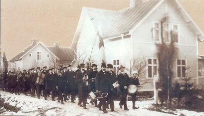 Flaggtåg på gata framför byggnader
Nyckelord: Flagga Musikinstrument