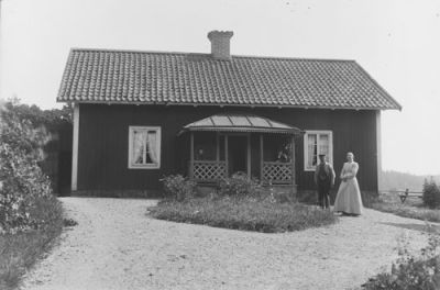 Man och kvinna stående på gårdsplan framför byggnad
