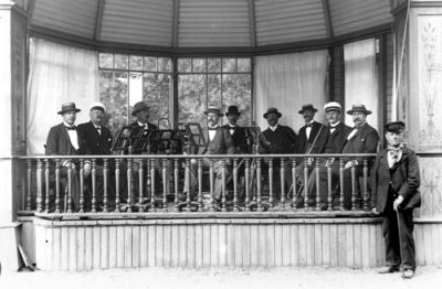 Mansorkester sittande på musikestrad
Nyckelord: Notställ Musikinstrument