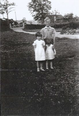 Pojke och 2 flickor stående på gräsmatta
