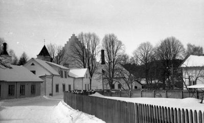 Snöig väg kantad med staket och med hus i bakgrunden
