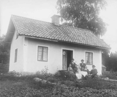 3 kvinnor 3 män och 1 flicka framför hus på landet
Nyckelord: Dräkt Gärdesgård