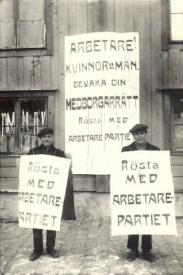 2 män med plakat framför byggnad
Nyckelord: Plakat