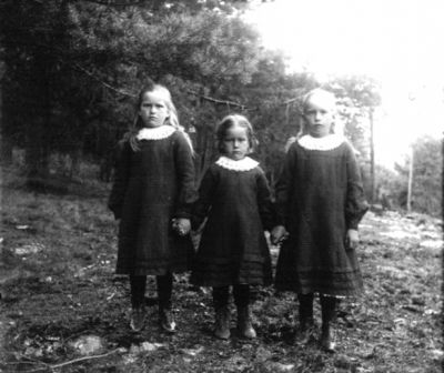 3 flickor stående i skogsbacke
