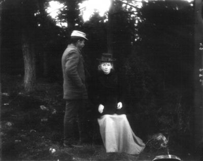 Stående man och sittande kvinna i skogen
