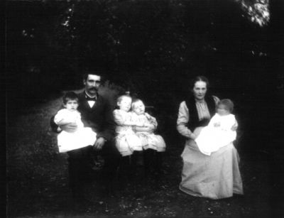 Man kvinna och 4 barn sittande på gårdsplan
