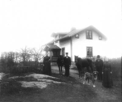 2 män 2 kvinnor 2 hästar och 1 hund framför byggnad
Nyckelord: Häst Hund