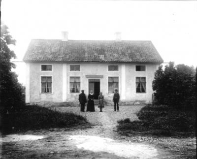 2 män 1 kvinna och 1 flicka på grusgård framför hus
Keywords: Hus