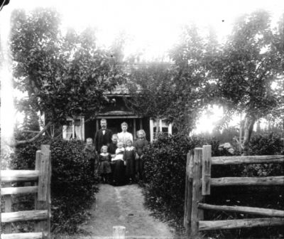 1 man 2 kvinnor och 5 barn på grusgång framför hus
