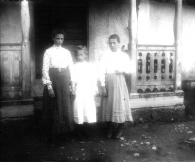 Kvinna och 2 flickor stående framför veranda
Nyckelord: Dräkt