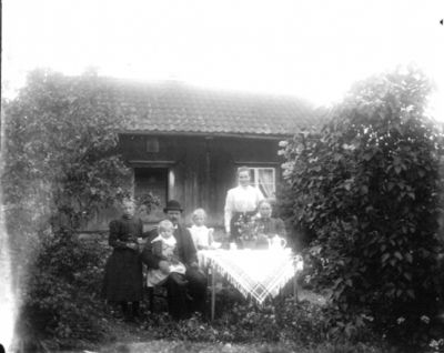 1 man 2 kvinnor och 3 barn runt trädgårdsbord framför byggnad
Nyckelord: Kaffekanna 