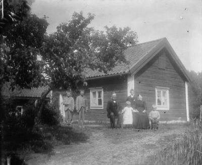 Man kvinna och 5 barn framför byggnad

