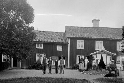 5 män 2 kvinnor 1 pojke och 1 hund framför hus
Nyckelord: Hund