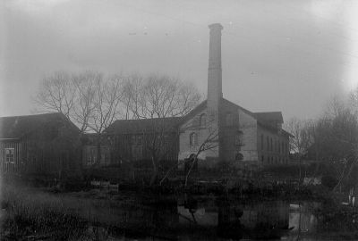 Fabriksbyggnad vid vattendrag
Nyckelord: Skorsten Vatten