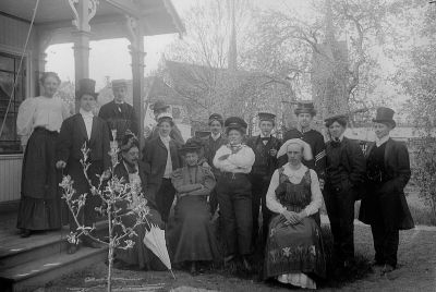 Högtidsklädda män och kvinnor utanför byggnad
Nyckelord: Dräkt Hatt Klockkedja Handklaver