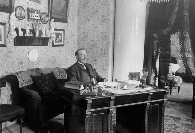 Man vid skrivbord
Nyckelord: Skrivbord Pokal Kakelugn Tapet Draperi Bläckhorn