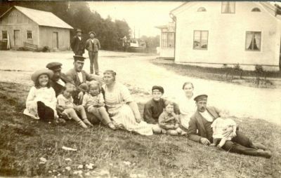 Män kvinnor och barn sittande på gräsmatta framför byggnad
