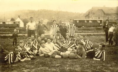 Fotbollslag sittande på plan med tåg i bakgrunden
