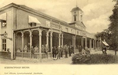 Ett stort antal människor på veranda till stor tornförsedd byggnad
