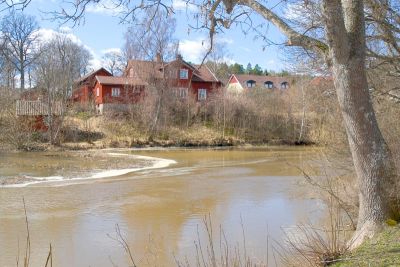 Rött hus på höjd invid vattendrag
