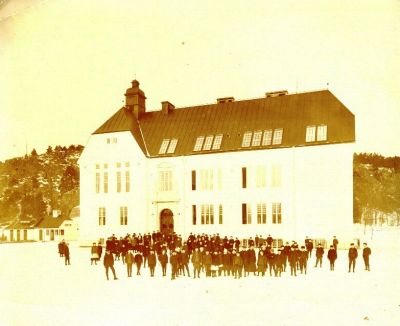 Elever på skolgård framför skolbyggnad
